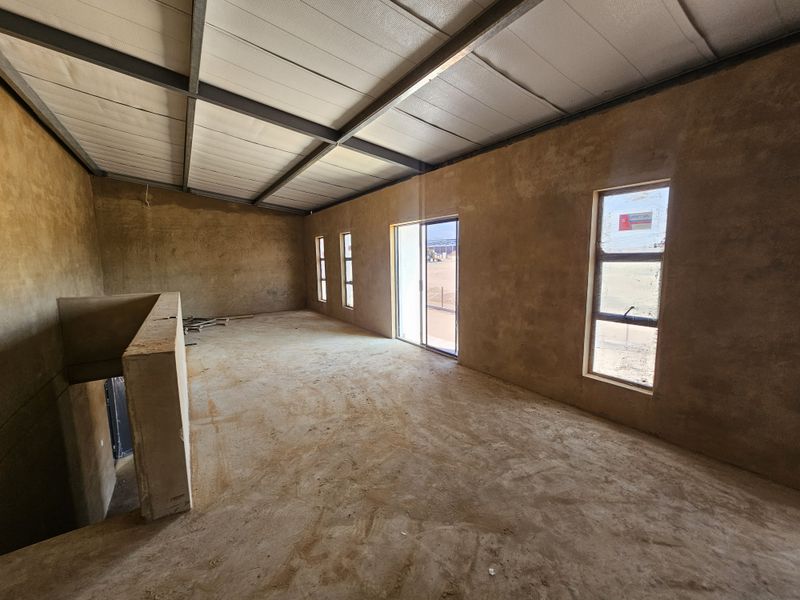 Spacious open-plan industrial interior in shell condition, featuring exposed steel roof beams, large windows, and a sliding door leading to an outdoor area.
