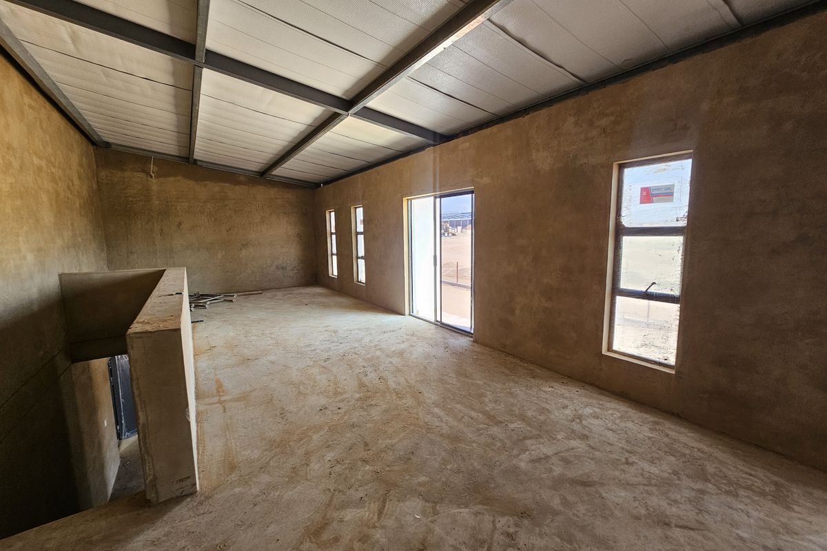 Spacious open-plan industrial interior in shell condition, featuring exposed steel roof beams, large windows, and a sliding door leading to an outdoor area.
