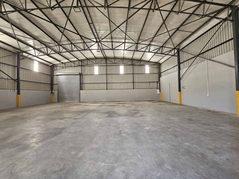 Spacious industrial warehouse unit featuring high-clearance steel truss roofing, concrete flooring, and a large roller shutter door for efficient access.