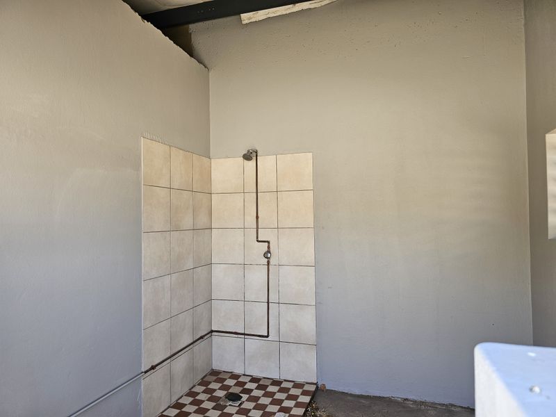 A basic industrial-style shower area featuring exposed copper plumbing, tiled shower enclosure, and unfinished wall surfaces.