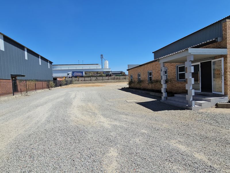 Industrial property featuring a brick office building, metal-clad warehouse structure, and a spacious gravel yard with secure perimeter fencing.