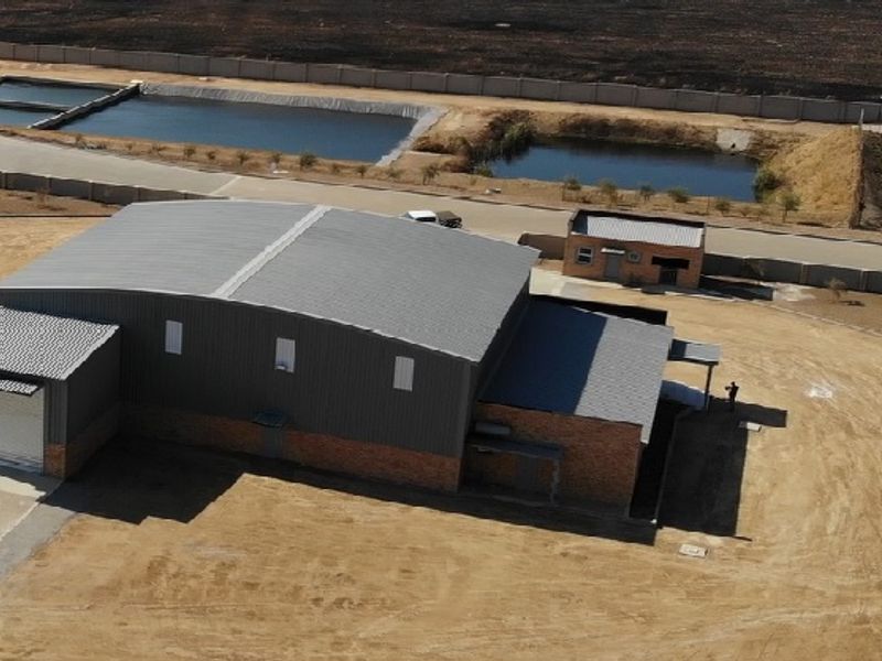 Aerial view of an industrial warehouse property featuring a metal roof, roller shutter door, and brick exterior walls within a fenced site.