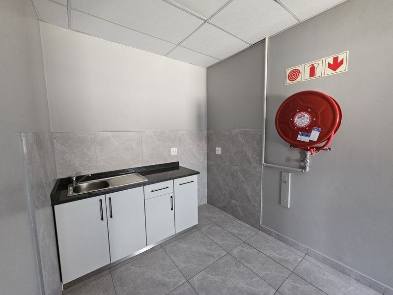 A clean utility space featuring built-in cabinetry with a granite countertop, stainless steel sink, tiled finishes, and a wall-mounted fire hose reel.