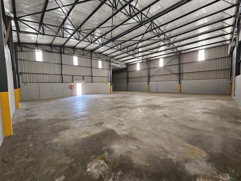 Spacious industrial warehouse unit featuring high exposed steel roof trusses, corrugated metal walls, and durable concrete flooring with emergency exit access.