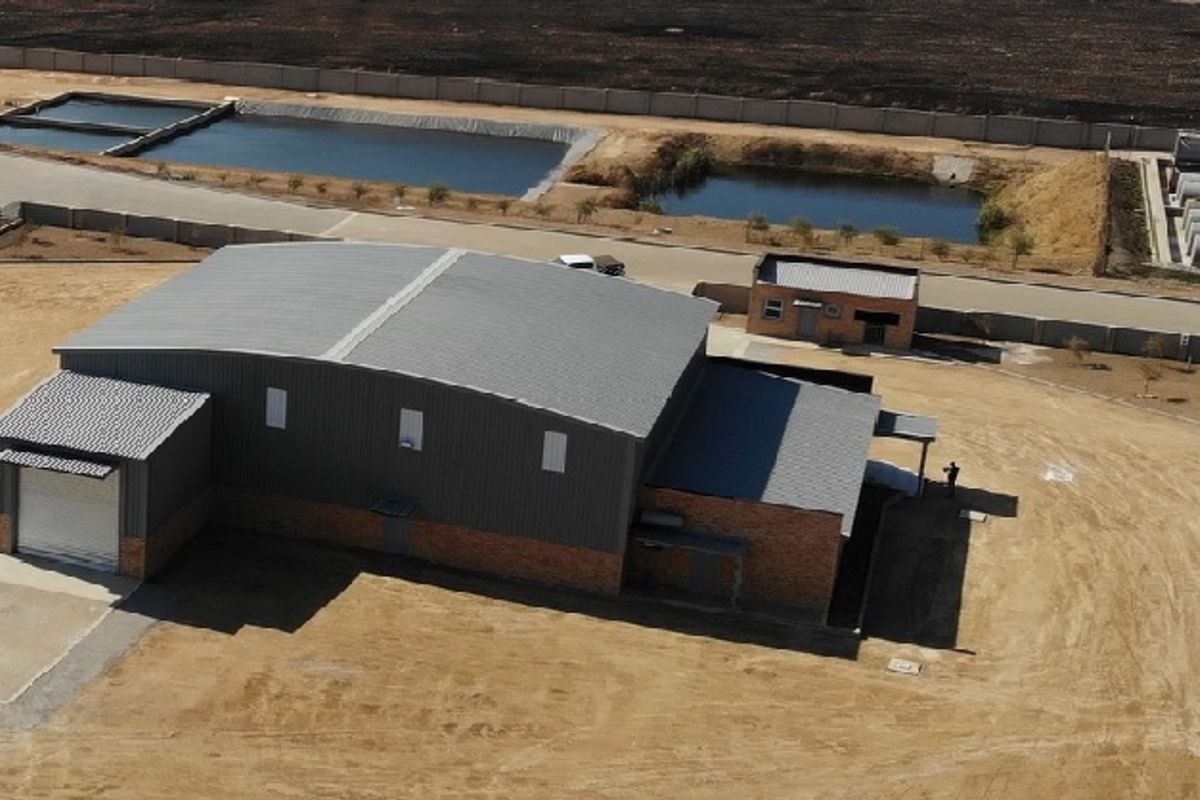 Aerial view of an industrial warehouse property featuring a metal roof, roller shutter door, and brick exterior walls within a fenced site.