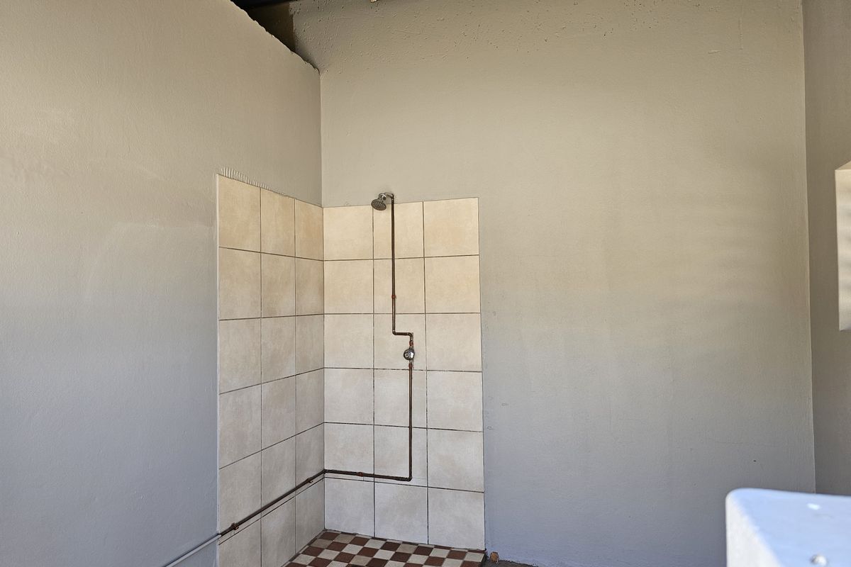 A basic industrial-style shower area featuring exposed copper plumbing, tiled shower enclosure, and unfinished wall surfaces.