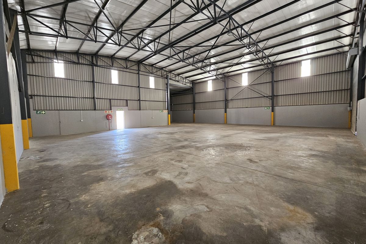 Spacious industrial warehouse unit featuring high exposed steel roof trusses, corrugated metal walls, and durable concrete flooring with emergency exit access.