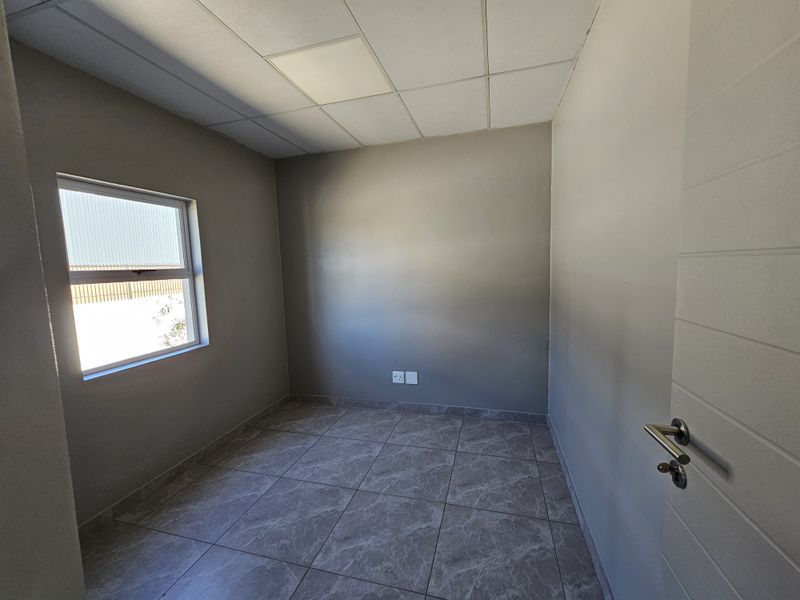 A clean, empty office space featuring modern tiled flooring, a suspended ceiling, and neutral wall finishes, suitable for a professional workspace.