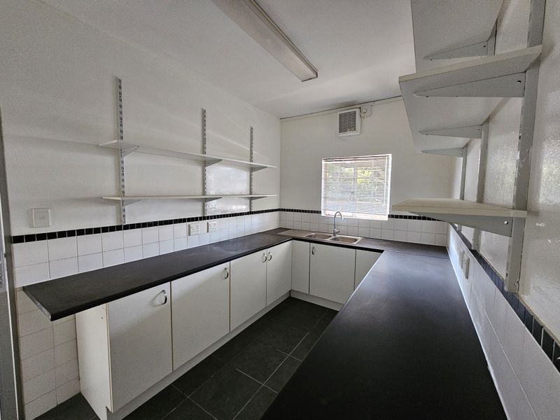 A clean, functional industrial-style kitchen featuring ample laminate counter space, double stainless steel sink, wall-mounted shelving, and tiled backsplash.