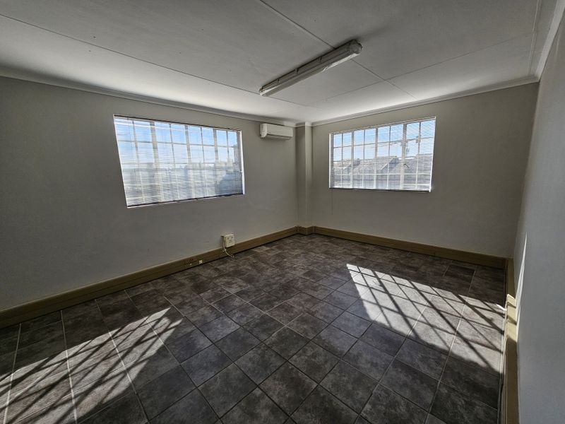 A vacant, well-lit office space featuring tiled flooring, split-system air conditioning, and dual windows, suitable for a professional workspace.
