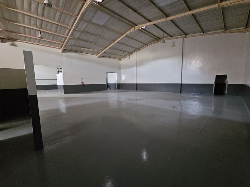 Spacious industrial warehouse unit featuring high ceilings with exposed steel trusses, durable epoxy-coated concrete flooring, and clean painted walls.