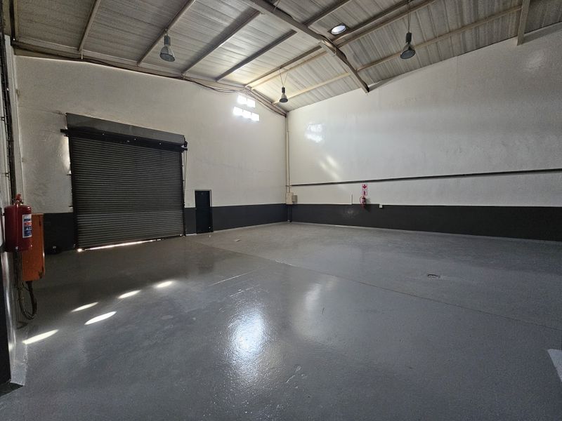 Spacious industrial warehouse unit featuring high ceilings with exposed steel trusses, durable epoxy-coated flooring, and a large roller shutter door for easy access.