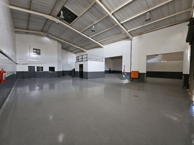 Spacious industrial warehouse unit featuring high ceilings with exposed steel trusses, polished epoxy flooring, and a mezzanine level for additional storage or office space.