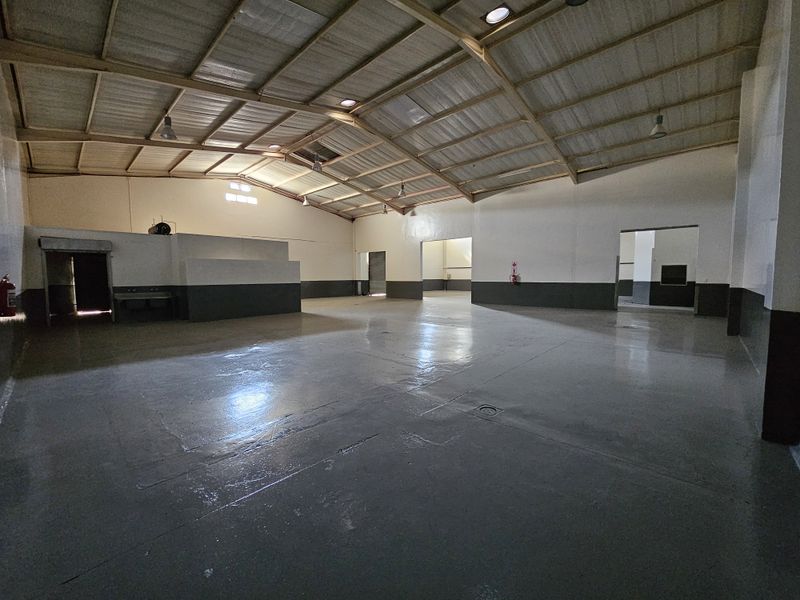 Spacious industrial warehouse unit featuring high ceilings with exposed steel trusses, durable painted concrete flooring, and multiple access points for efficient logistics.