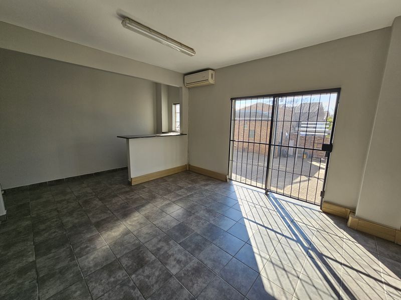 An open-plan living area featuring tiled flooring, a breakfast bar, a wall-mounted air conditioner, and a secure sliding glass door leading to the exterior.