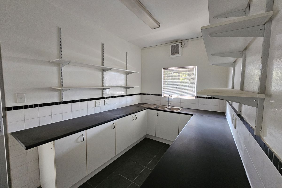 A clean, functional industrial-style kitchen featuring ample laminate counter space, double stainless steel sink, wall-mounted shelving, and tiled backsplash.