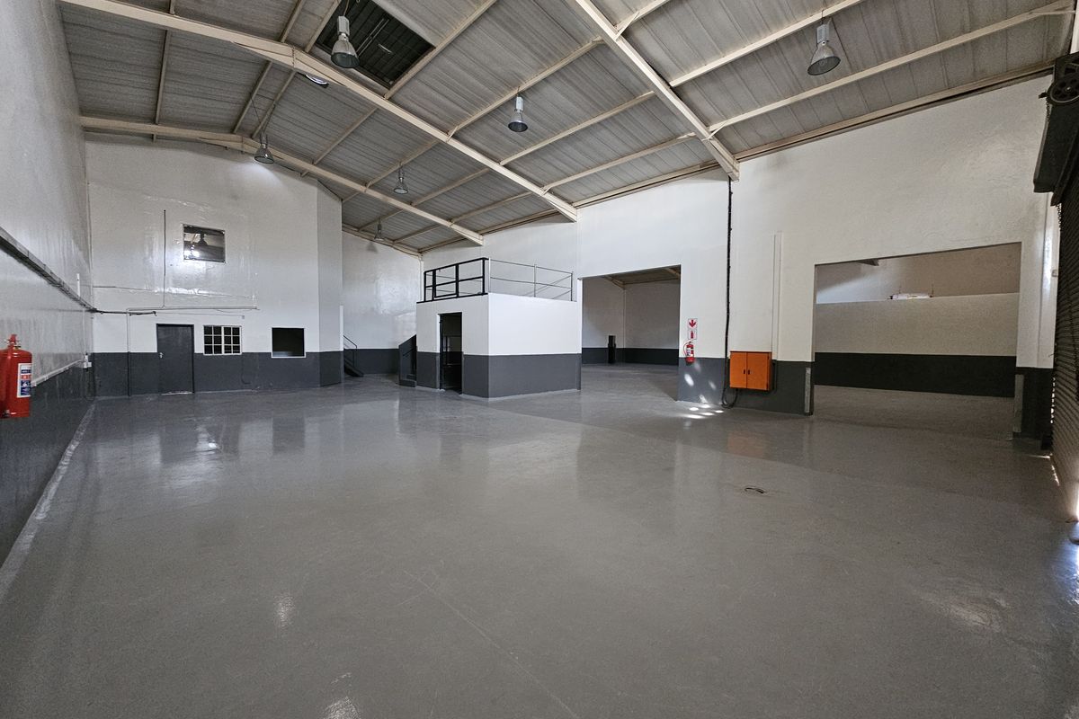 Spacious industrial warehouse unit featuring high ceilings with exposed steel trusses, polished epoxy flooring, and a mezzanine level for additional storage or office space.