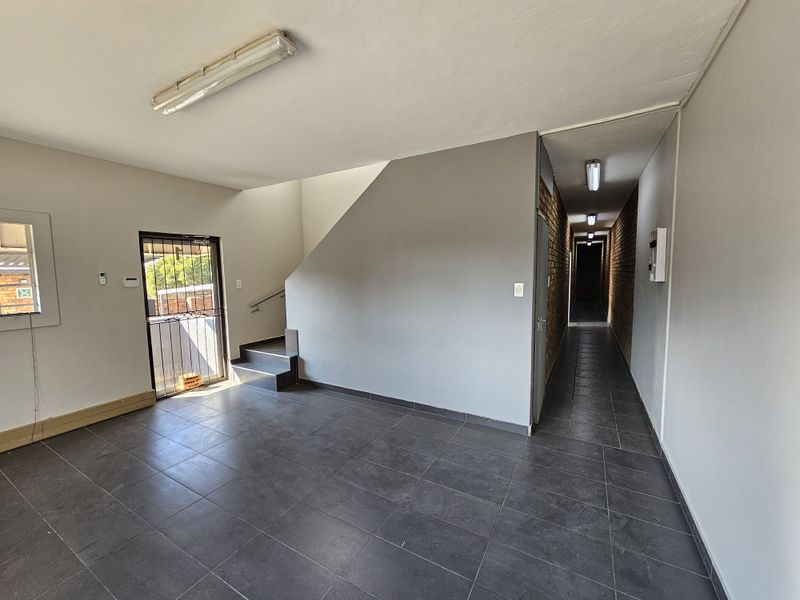 A spacious, tiled entrance area featuring a staircase and a long hallway with exposed brick accents, providing access to the industrial property's interior.