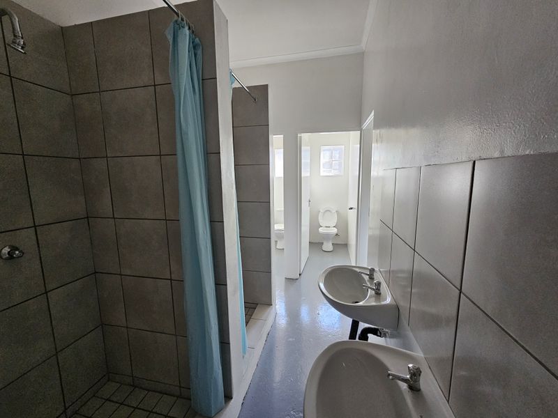 Functional industrial-style bathroom featuring tiled shower enclosures, dual pedestal wash basins, and separate toilet cubicles with basic finishes.