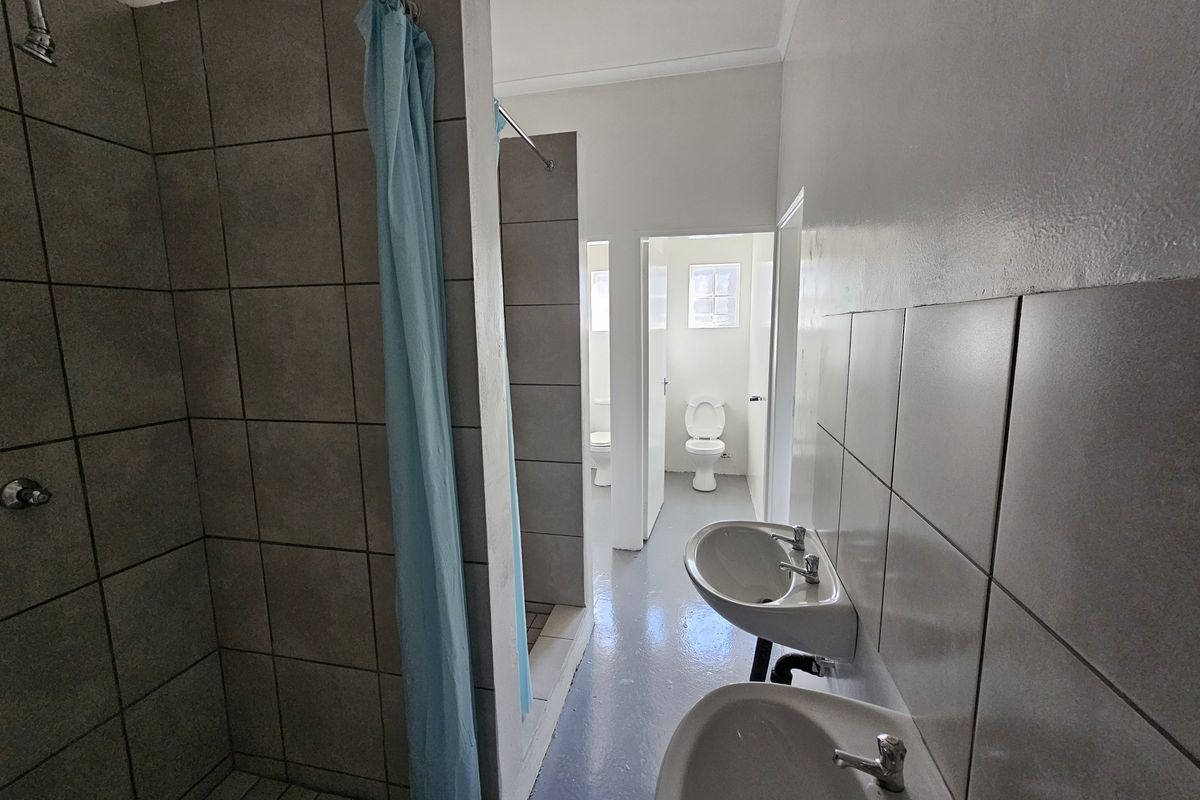 Functional industrial-style bathroom featuring tiled shower enclosures, dual pedestal wash basins, and separate toilet cubicles with basic finishes.