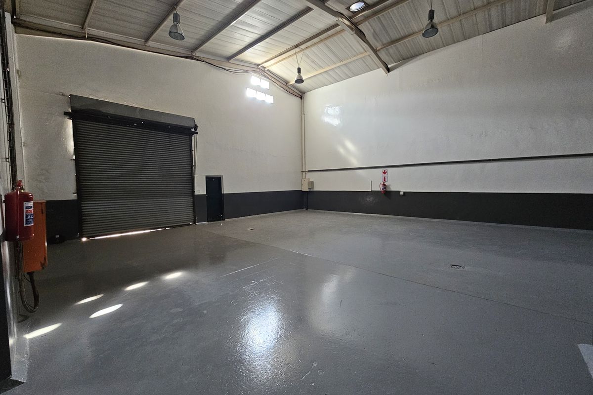 Spacious industrial warehouse unit featuring high ceilings with exposed steel trusses, durable epoxy-coated flooring, and a large roller shutter door for easy access.