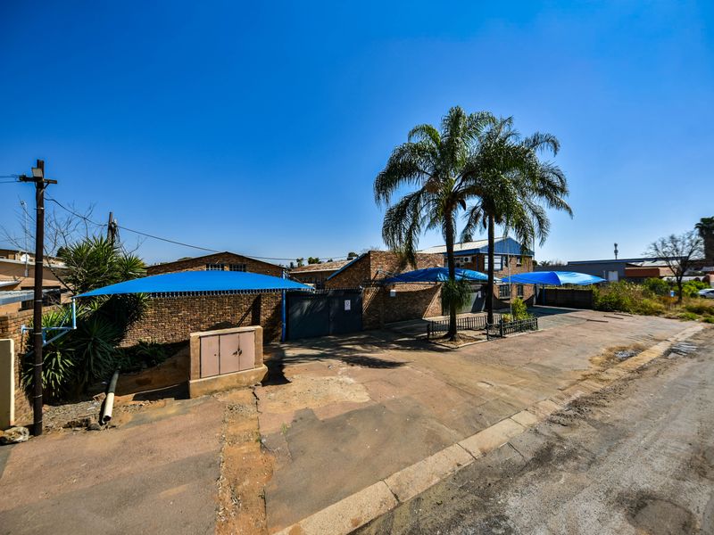 Front exterior view of an industrial property featuring a brick facade, paved driveway, and multiple shade cloth carports for vehicle parking.