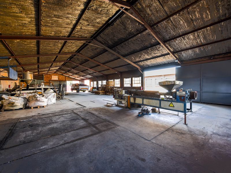 Spacious industrial warehouse featuring exposed steel roof trusses, concrete flooring, and large sliding access doors, suitable for manufacturing or storage operations.