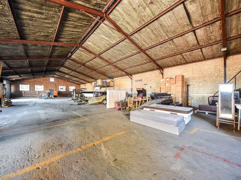 Large industrial warehouse space featuring exposed steel roof trusses, concrete flooring, and brick walls, suitable for storage or workshop use.