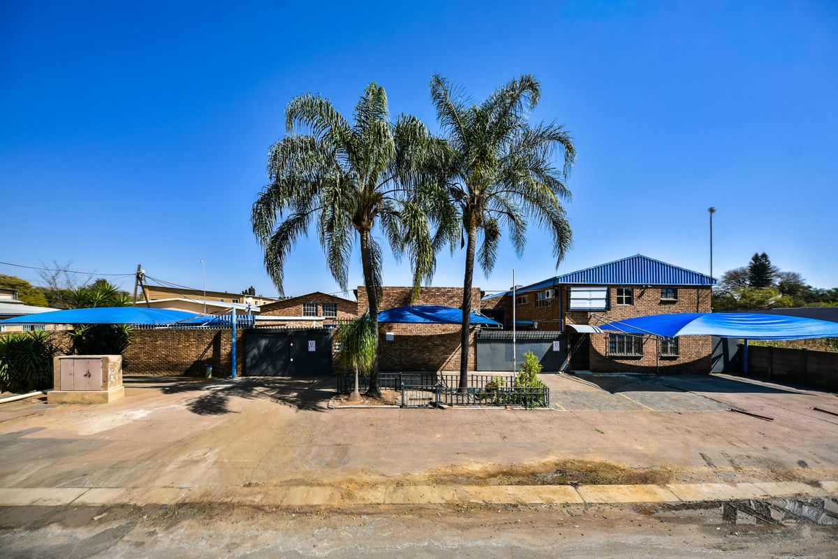 Front exterior view of an industrial property featuring a brick facade, metal roofing, paved driveway, and multiple shade cloth parking structures.
