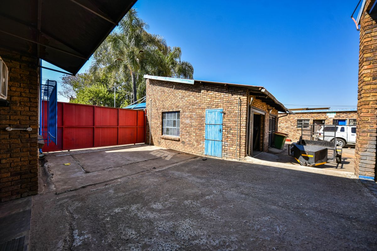 Rear exterior view of an industrial property featuring face brick construction, a concrete yard area, and secure metal gate access.