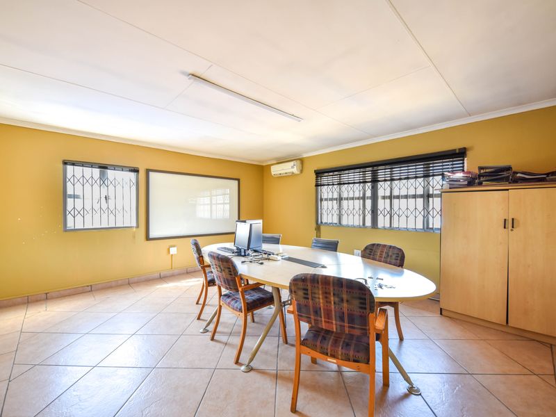 A functional office space featuring tiled flooring, security bars on windows, a wall-mounted air conditioner, and a built-in whiteboard.