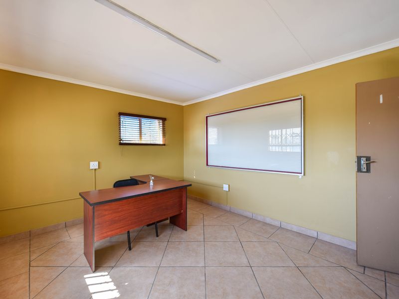A functional office space featuring tiled flooring, a wall-mounted whiteboard, and natural light provided by a window with venetian blinds.