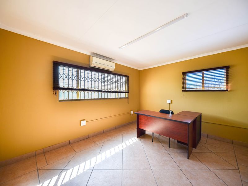 A functional office space featuring tiled flooring, security bars on windows, and a wall-mounted air conditioning unit.