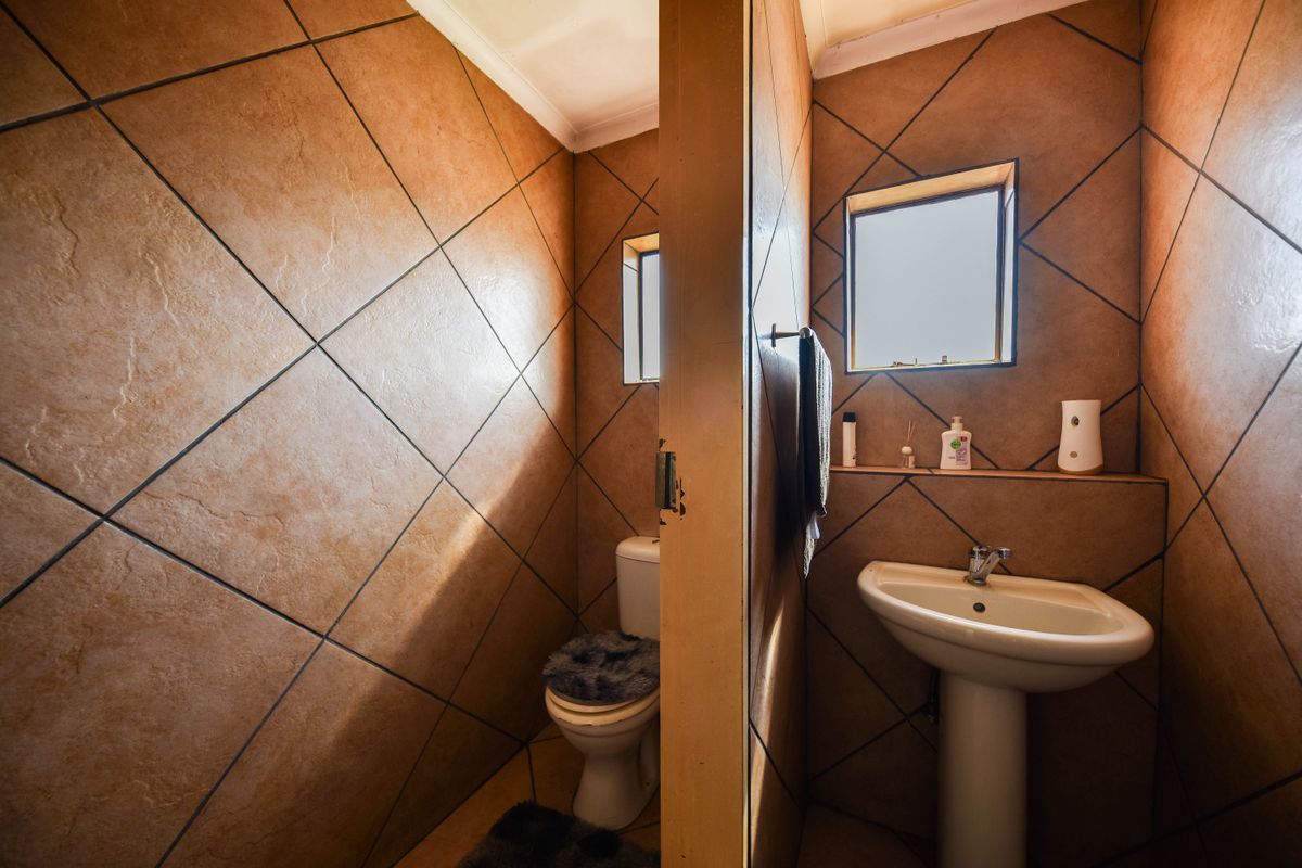 A functional bathroom featuring tiled walls and flooring, equipped with a pedestal washbasin and a toilet.
