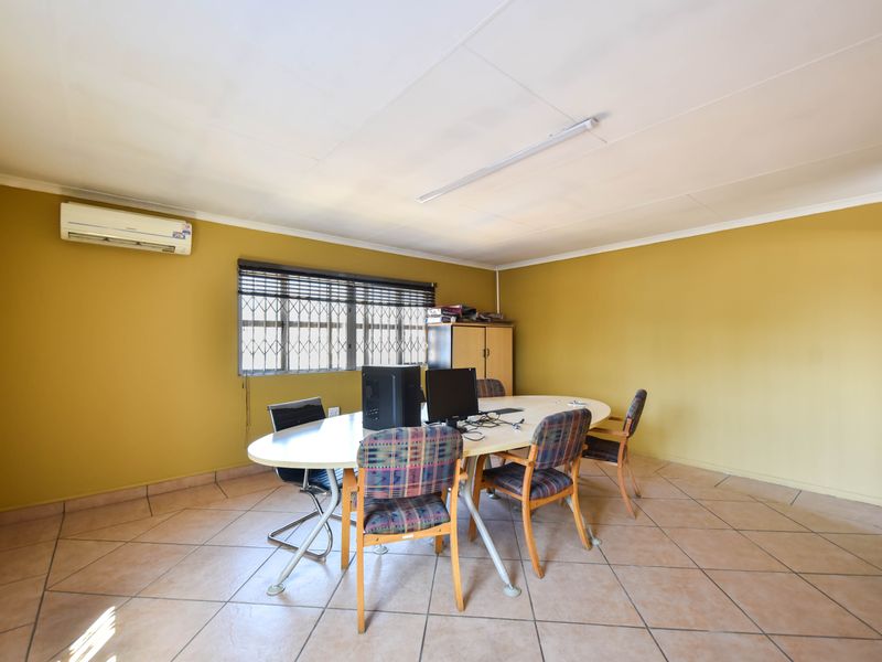 A functional office space featuring tiled flooring, a wall-mounted air conditioning unit, and security bars on the window.