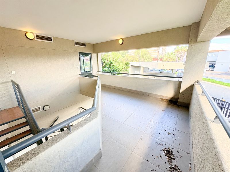 An open-air balcony or landing area featuring tiled flooring, metal safety railings, and a staircase, providing access to the office building levels.