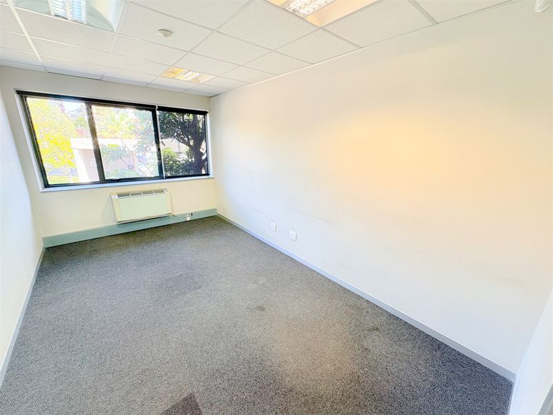 A vacant office space featuring a suspended ceiling, recessed lighting, carpeted flooring, and a wall-mounted air conditioning unit.