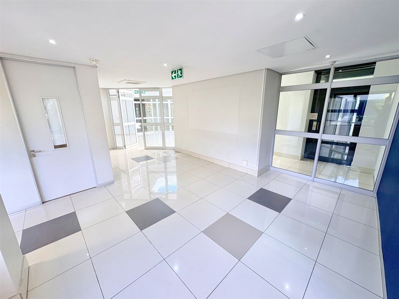 A bright and modern office entrance lobby featuring polished tiled flooring, recessed lighting, and secure aluminium-framed glass partitioning.