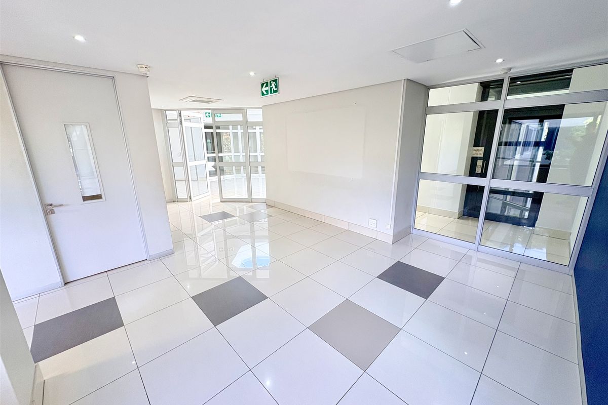 A bright and modern office entrance lobby featuring polished tiled flooring, recessed lighting, and secure aluminium-framed glass partitioning.