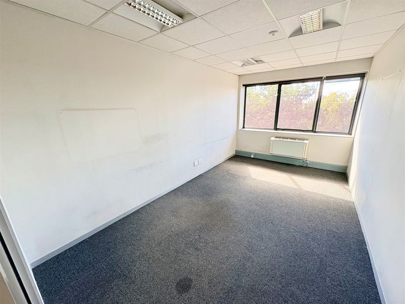 A vacant office space featuring a suspended ceiling, recessed lighting, carpeted flooring, and a window-mounted air conditioning unit.