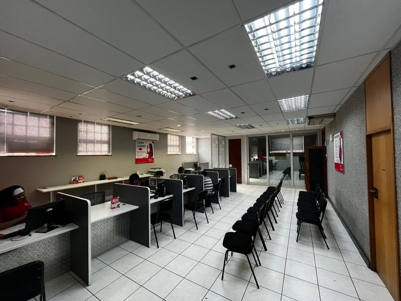 Commercial office space featuring a row of built-in workstations, suspended acoustic ceiling tiles, recessed fluorescent lighting, and tiled flooring.