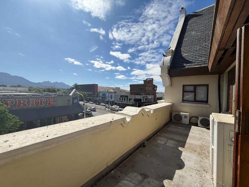 An elevated balcony area overlooking the street, featuring a parapet wall, tiled roof section, and external air conditioning units.