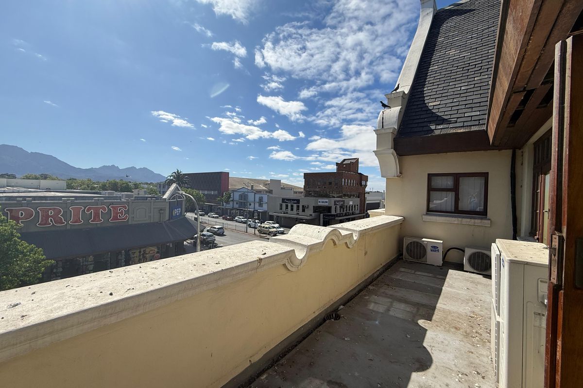 An elevated balcony area overlooking the street, featuring a parapet wall, tiled roof section, and external air conditioning units.