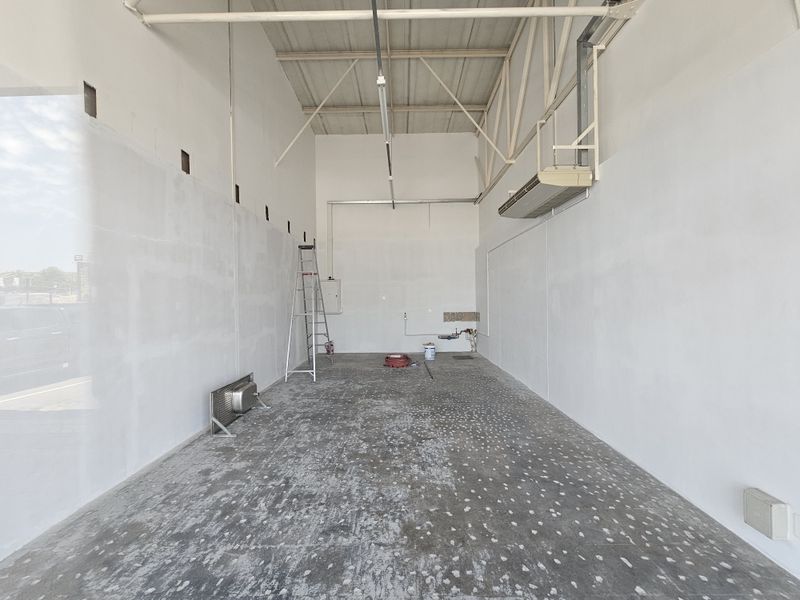 An empty retail space featuring high ceilings with exposed trusses, wall-mounted HVAC unit, and unfinished concrete flooring, ready for custom fit-out.