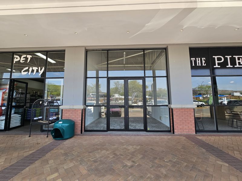 Front facade of a retail unit featuring large glass display windows, double glass entrance doors, and brickwork detailing under a covered walkway.