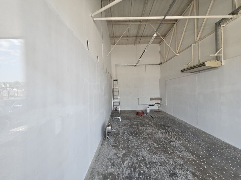 An empty retail space featuring high ceilings with exposed trusses, concrete flooring, and basic utility connections, suitable for custom fit-out.