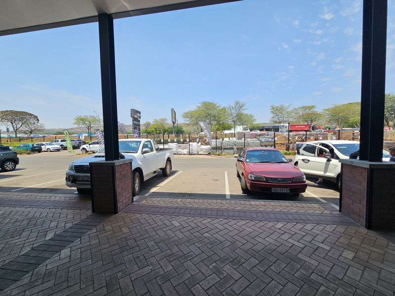 View from a covered retail walkway looking out over a paved parking area with brick-column supports.
