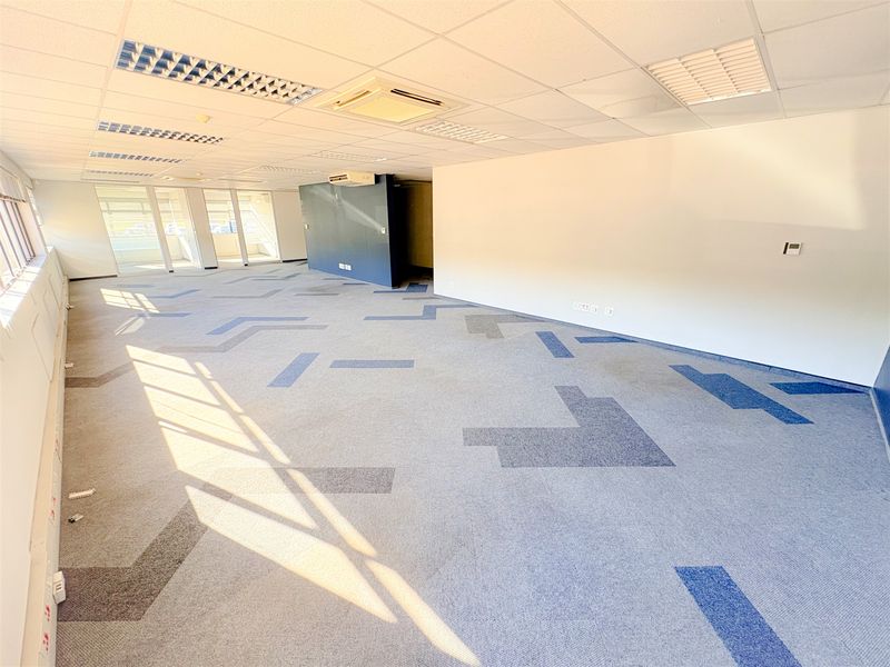 A spacious, open-plan office area featuring suspended ceilings, recessed lighting, ducted air conditioning, and large windows providing ample natural light.