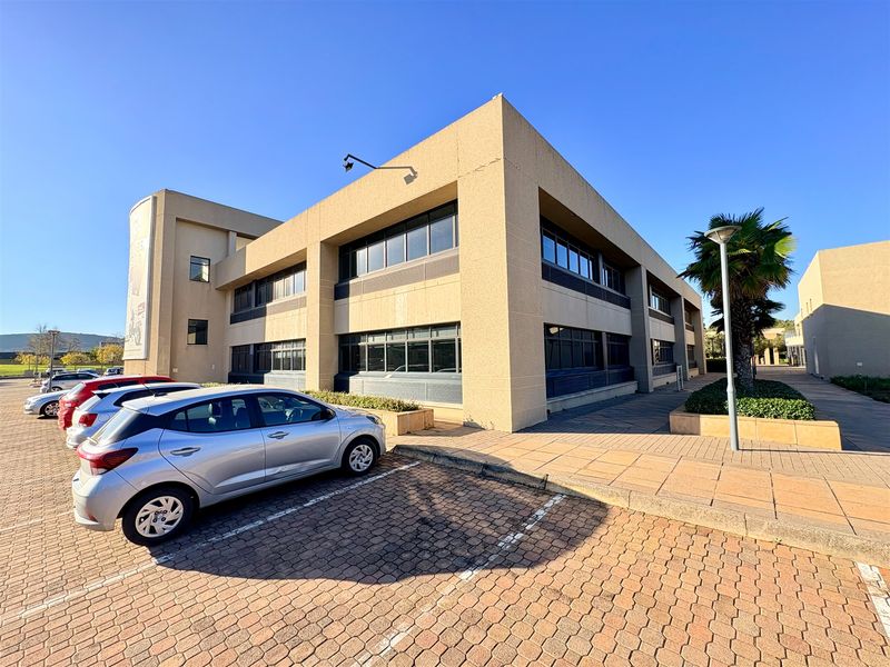 Exterior view of a multi-story commercial office building featuring a paved parking area and modern aluminum-framed windows.