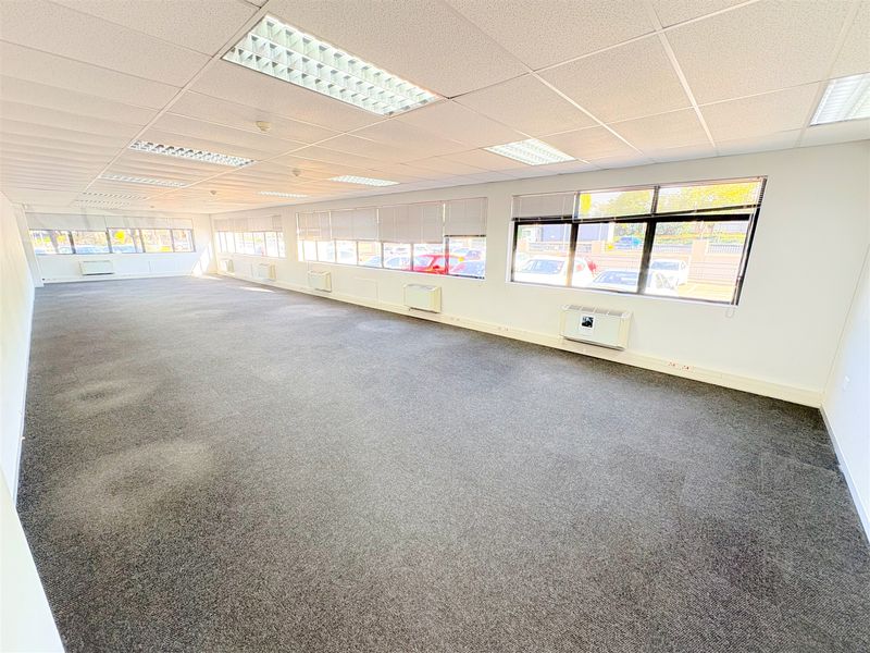 Spacious, open-plan office area featuring suspended ceilings, recessed lighting, wall-mounted air conditioning units, and large windows providing ample natural light.